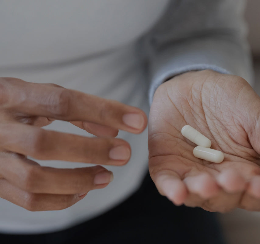 Eine Person hält zwei weiße Nahrungsergänzungsmittel in der Hand und bereitet sich darauf vor, sie einzunehmen. Die Hände sind gut sichtbar, während der Hintergrund unscharf ist.